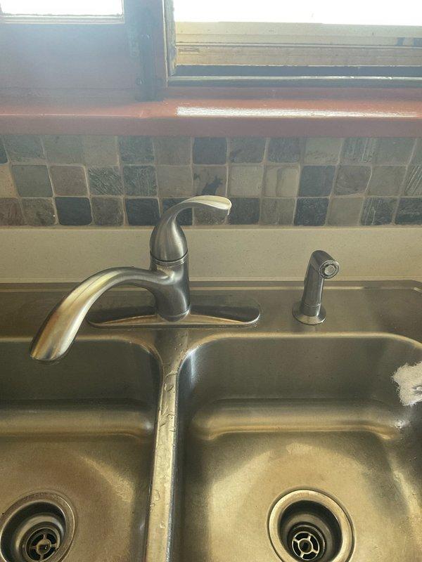 Responded to service call for kitchen and bathroom faucet repairs in 90-year-old residential property. Upon arrival, inspected kitchen double-basin stainless steel sink with single-handle faucet and separate pull-out side sprayer. Evaluated faucet operation, tested water flow, and checked for leaks at connections and base mounting. Proceeded to bathroom where exposed copper supply lines and shut-off valves were visible due to deteriorated wall conditions. Assessed plumbing infrastructure including vertical copper piping with brass fittings and valves. Performed necessary repairs to restore proper faucet function in both locations, addressing issues common in aging plumbing systems. Documented conditions with photographs for service records.