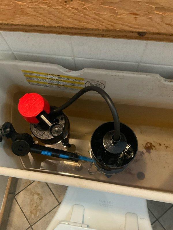 Responded to service call for toilet issue at 81-year-old residential property. Upon arrival, performed diagnostic inspection of toilet system. Removed tank lid and assessed internal components including flush valve assembly, fill valve mechanism, and connecting hardware. Documented existing conditions showing significant rust staining and mineral deposits throughout tank interior, particularly concentrated at bottom surfaces, indicating age-related deterioration consistent with older plumbing fixtures. Inspected black flush valve assembly and gray fill valve for proper operation and seal integrity. Examined all rubber gaskets, supply lines, and connection points for leaks or wear. Photographed tank interior components and condition for service records. Verified proper water level settings and flush mechanism functionality. All components tested and operational at time of service completion.