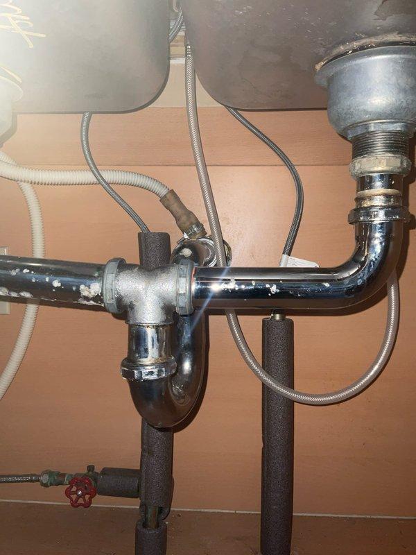 Completed installation of kitchen faucet using customer-supplied fixtures beneath double-bowl sink. Connected chrome-plated P-trap drainage assembly with T-configuration to accommodate dual drains, installed flexible supply lines with braided stainless steel hoses, and verified proper water shut-off valve operation. Applied foam pipe insulation to vertical supply lines to prevent condensation, tested all connections for leaks, and confirmed proper drainage flow through both basins.