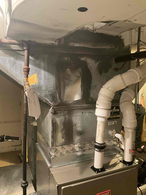 Conducted on-site evaluation for HVAC system replacement on a 13-year-old Bryant furnace unit exhibiting severe fire and smoke damage. The furnace showed extensive soot accumulation, discoloration, and burn marks across the upper cabinet section and front panel, indicating a significant heat event or combustion malfunction. Ceiling damage above the unit revealed structural exposure consistent with overheating or exhaust failure. Documented existing system configuration including white PVC condensate drain and venting lines, copper refrigerant piping with visible connections, and current ductwork layout. Photographed equipment conditions, surrounding utility space constraints, and adjacent water heater for comprehensive replacement planning. Provided detailed estimate for complete HVAC system replacement to address fire-damaged equipment and restore safe, efficient heating and cooling operation.