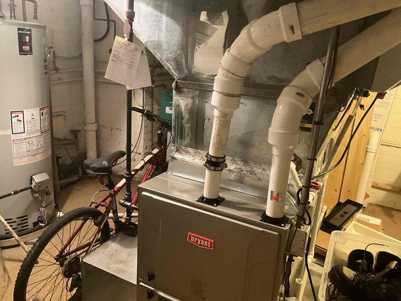 Conducted on-site evaluation for HVAC system replacement on a 13-year-old Bryant furnace unit exhibiting severe fire and smoke damage. The furnace showed extensive soot accumulation, discoloration, and burn marks across the upper cabinet section and front panel, indicating a significant heat event or combustion malfunction. Ceiling damage above the unit revealed structural exposure consistent with overheating or exhaust failure. Documented existing system configuration including white PVC condensate drain and venting lines, copper refrigerant piping with visible connections, and current ductwork layout. Photographed equipment conditions, surrounding utility space constraints, and adjacent water heater for comprehensive replacement planning. Provided detailed estimate for complete HVAC system replacement to address fire-damaged equipment and restore safe, efficient heating and cooling operation.