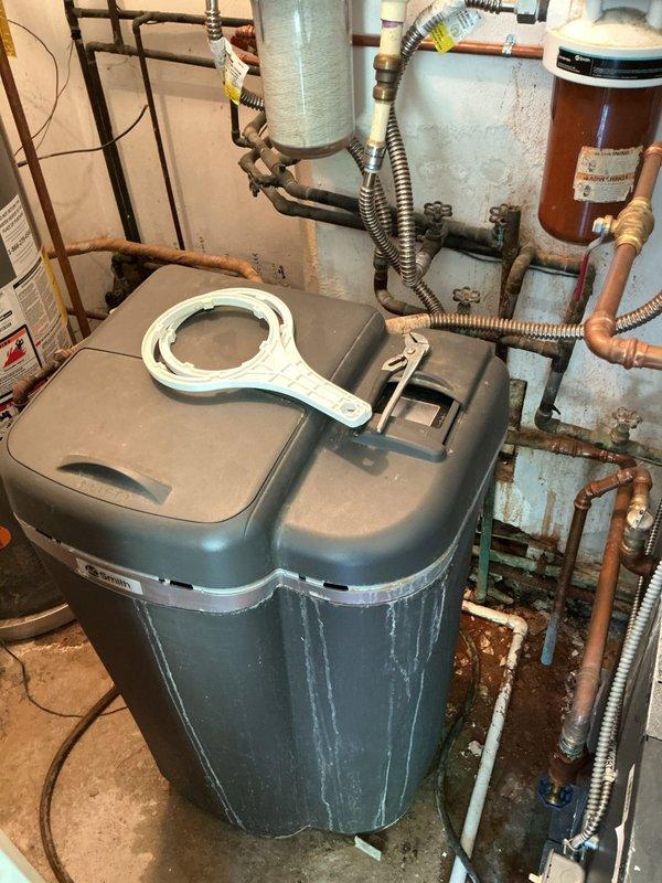 Responded to low water pressure complaint at 60-year-old residential property. Upon inspection of mechanical room, identified sediment buildup in dual water filter housings as primary cause of reduced flow. Removed and replaced both filter cartridges in white cylindrical housings connected to copper supply lines. Inspected water softener system for proper operation and verified brine tank levels were adequate. Checked pressure tank and expansion tank connections for proper function. Flushed sediment from copper piping system and tested pressure at multiple fixtures throughout home. Verified all valves in supply line were fully open and operating correctly. Restored water pressure to normal operating range. Recommended establishing regular filter replacement schedule every 3-6 months to prevent future pressure loss issues. System tested and functioning properly at completion.