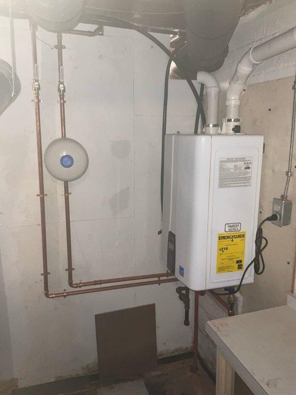 Removed and replaced existing water heating system with new Navien tankless water heater featuring integrated recirculation pump and internal buffer tank. Installed new S5 2.1 gallon expansion tank in conjunction with tankless unit to accommodate thermal expansion in closed plumbing system. Configured copper supply lines, PVC venting system, and electrical connections per manufacturer specifications. Unit mounted to wall in basement utility area with proper clearances maintained for service access and ventilation requirements.