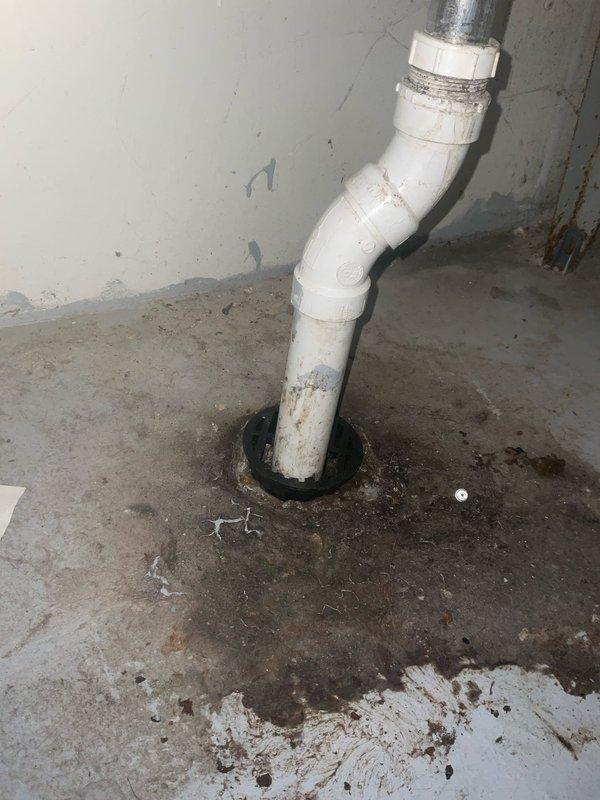 Replaced deteriorated cast iron cleanout cap on basement floor drain with new PVC assembly. The existing drain showed significant corrosion and staining around the floor penetration, with the original cast iron cap requiring replacement due to age and wear. Installed new white PVC piping with proper fittings and elbow connections to restore functionality and provide reliable access for future maintenance.