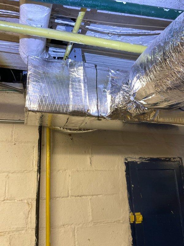 Responded to report of water leak in basement with pooling in unspecified location. Conducted thorough inspection of 100-year-old home's basement and utility areas to identify moisture source. Examined exposed plumbing lines, gas piping, and HVAC infrastructure including ductwork and insulation throughout basement ceiling space. Inspected condition of foil-faced insulation wrapped around rectangular supply ducts and flexible ductwork connections for signs of condensation or moisture accumulation. Verified proper insulation installation and checked for potential condensation issues on cold air supply lines that could cause water pooling. Performed routine air conditioning system evaluation as requested, examining duct integrity and insulation sealing at connection points. Documented findings with photographic evidence of basement infrastructure, HVAC components, and insulation condition for reference.