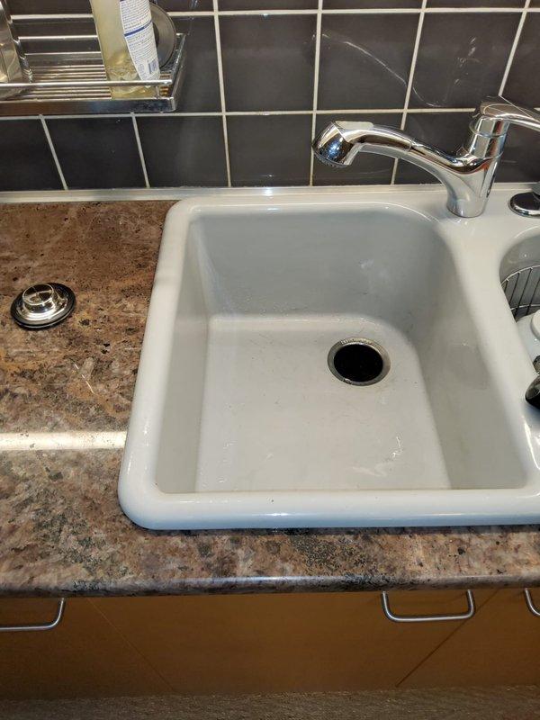 Responded to garbage disposal issue in century-old home. Upon arrival, inspected kitchen sink and under-sink plumbing configuration. Found black garbage disposal unit properly mounted to white rectangular single-basin sink with chrome faucet and standard PVC drainage assembly. Verified disposal mounting flange connection at sink drain, checked electrical wiring and power supply, and examined discharge plumbing including black elbow joint connecting to white PVC drain lines. Inspected dishwasher drain hose connection, water supply lines with braided flex connectors, and cleanout access point. Tested disposal operation and confirmed proper function of all components. System operating normally with no leaks detected at time of service completion.