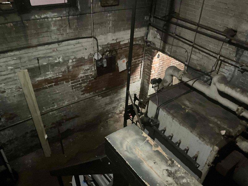 Conducted comprehensive site assessment for commercial steam boiler replacement in industrial mechanical room with exposed brick walls and concrete flooring showing moisture damage. Evaluated existing equipment condition, documented deteriorated cylindrical boiler component with visible rust and corrosion, assessed piping infrastructure and structural supports, and photographed installation environment including access stairwell. Provided detailed estimate for complete boiler system replacement.