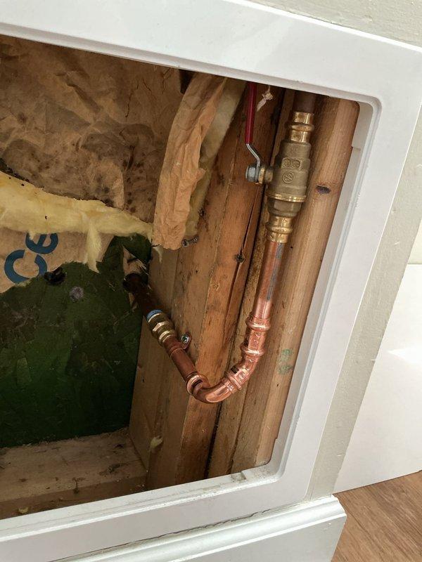Responded to service call for severely leaking outdoor spigot. Accessed water supply line through interior wall panel to locate and address source of leak. Inspected copper supply piping, compression fittings, and brass shut-off valve with red handle located between floor joists. Evaluated exterior hose bib mounted on building siding and verified connection integrity where green garden hose was attached. Completed necessary repairs to eliminate water leak and restore proper function to outdoor water spigot system.