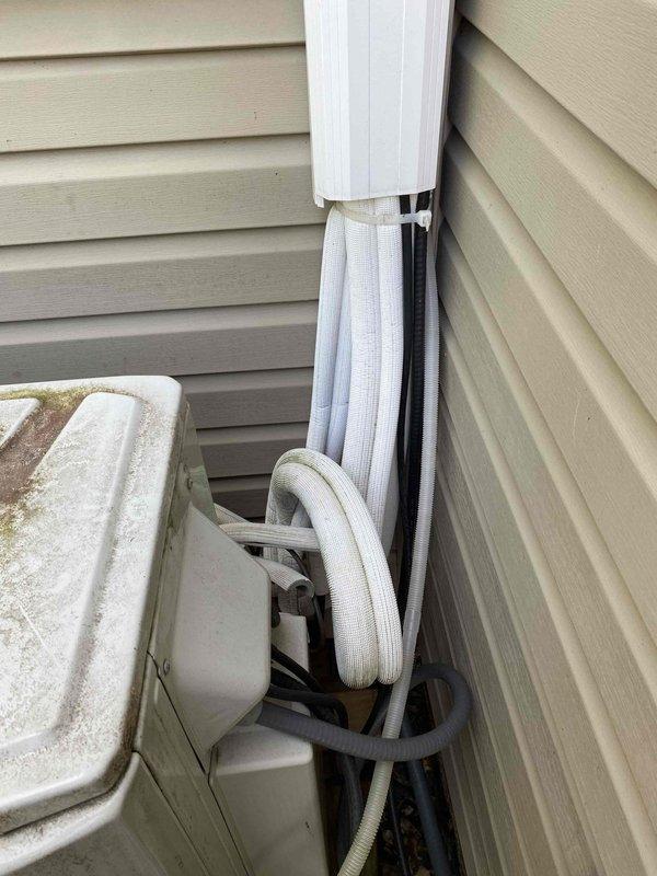 Responded to service call for three-year-old mini split air conditioning system not cooling properly. Upon arrival, performed diagnostic inspection of both indoor and outdoor units. Inspected refrigerant line set, condensate drainage system, and electrical connections visible at exterior installation. Verified proper operation of condensate drain line and checked for any visible obstructions or damage to refrigerant lines running along building exterior. Evaluated outdoor unit mounting and line set routing for any potential issues affecting system performance. Documented equipment condition with photographs showing exterior components including line set installation, utility disconnect box, and condensate drain configuration.