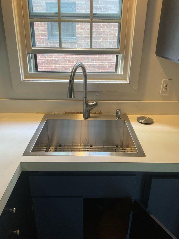 Completed installation of new kitchen sink and faucet assembly, including undermount stainless steel sink basin with chrome pull-down spray faucet and integrated soap dispenser. Installed Contractor-brand garbage disposal unit with proper mounting hardware and electrical connections. Connected all drain lines using white PVC piping and established proper waste line configuration from disposal to existing drainage system. Verified all water supply connections to hot and cold lines, tested faucet operation and spray head functionality, and confirmed garbage disposal operates without leaks or unusual noise. All components secured and tested successfully.