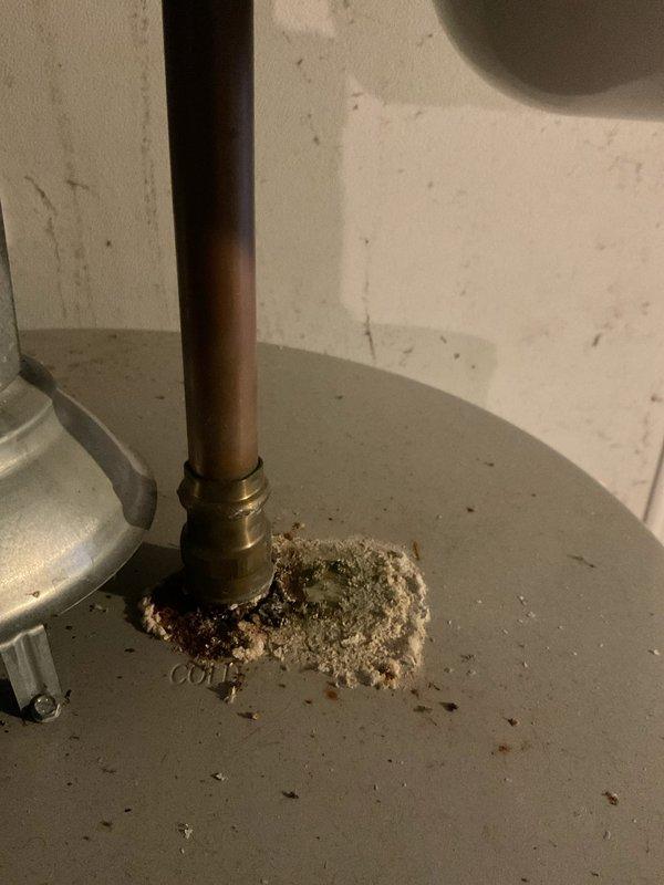 Responded to service call for intermittent water dripping from pipe with valve on side of 2-year-old hot water heater. Upon inspection, identified significant mineral deposit and sediment accumulation around brass fitting at copper pipe connection point on top of tank. Documented condition of water heater connections, mineral buildup at pipe junction, and overall mechanical room plumbing configuration including overhead piping system. Completed diagnostic evaluation of dripping issue and photographed affected areas for assessment.
