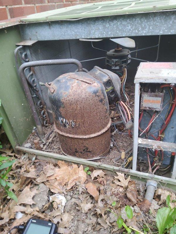 Completed scheduled recurring cooling maintenance service on outdoor air conditioning unit. Upon arrival, found unit operational but surrounded by overgrown vegetation including weeds, grasses, and climbing vines that had encroached significantly around the equipment. Removed access panel for internal inspection and discovered compressor exhibiting extensive rust coverage across entire cylindrical surface, indicating advanced age and prolonged weather exposure. Documented equipment condition through photographs showing heavily corroded compressor, coil assembly, electrical control components with exposed wiring, and fan motor assembly. Unit's green metal housing also displayed signs of aging and outdoor element exposure. Cleared immediate area of fallen leaves and debris. Verified unit operation and confirmed cooling system functionality despite visible deterioration of internal components. Recommended monitoring compressor condition closely due to extensive corrosion and considering v