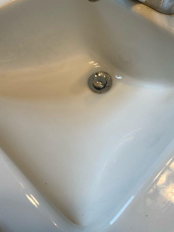 Completed partial removal and replacement of drainage system components over a day and a half period with helper assistance. Removed existing drain assembly and installed new white PVC vertical waste line with cleanout access port, including proper T-joint configuration and floor-level adapter fitting. Replaced sink drain stopper assembly with chrome-finished fixture. System tested and verified operational, with final completion pending.