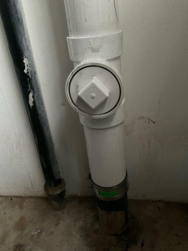 Completed partial removal and replacement of drainage system components over a day and a half period with helper assistance. Removed existing drain assembly and installed new white PVC vertical waste line with cleanout access port, including proper T-joint configuration and floor-level adapter fitting. Replaced sink drain stopper assembly with chrome-finished fixture. System tested and verified operational, with final completion pending.