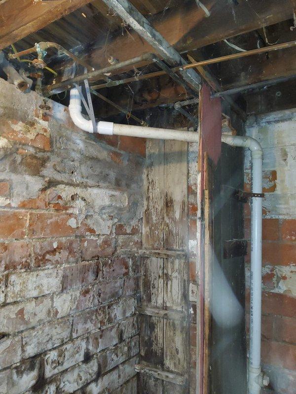 Responded to service call for leaking PVC joint in basement of older residential property. Upon arrival, inspected plumbing system and identified compromised joint connection on white PVC drainage piping mounted to ceiling joists in basement area. Basement showed signs of previous moisture intrusion with visible water staining on brick walls and wooden structural elements. Assessed under-sink plumbing configuration connected to Badger 100 garbage disposal unit to verify drainage system integrity. Repaired defective PVC joint using appropriate coupling and PVC cement to ensure watertight seal. Tested repaired connection for leaks by running water through system and verified proper drainage flow. Inspected surrounding plumbing for additional potential failure points given age of structure. All connections secured and functioning properly upon completion.