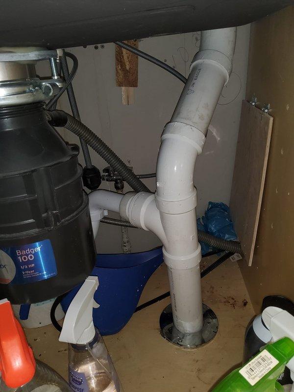 Responded to service call for leaking PVC joint in basement of older residential property. Upon arrival, inspected plumbing system and identified compromised joint connection on white PVC drainage piping mounted to ceiling joists in basement area. Basement showed signs of previous moisture intrusion with visible water staining on brick walls and wooden structural elements. Assessed under-sink plumbing configuration connected to Badger 100 garbage disposal unit to verify drainage system integrity. Repaired defective PVC joint using appropriate coupling and PVC cement to ensure watertight seal. Tested repaired connection for leaks by running water through system and verified proper drainage flow. Inspected surrounding plumbing for additional potential failure points given age of structure. All connections secured and functioning properly upon completion.