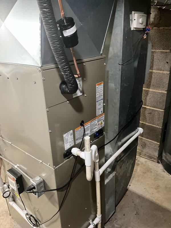 Completed full HVAC system installation including outdoor Bryant condenser unit mounted on new black plastic pad alongside exterior of residence. Installed new indoor evaporator coil in basement mechanical room, positioned adjacent to existing air handler unit. Ran refrigerant lines connecting outdoor condenser to indoor evaporator coil with proper insulation and securing. Installed new electrical disconnect box on exterior wall with conduit running from house to outdoor unit, ensuring all electrical connections meet code requirements. Added PVC condensate drain lines for proper moisture removal from system. Installed new programmable thermostat to provide enhanced temperature control and energy efficiency. Verified all refrigerant connections are secure, tested electrical components for proper voltage and amperage, and confirmed system operates within manufacturer specifications. All equipment properly labeled with safety and operational information.