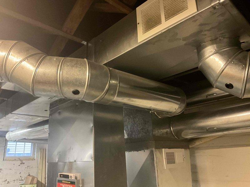 Completed estimate for ductwork replacement in basement utility area. Assessed existing metallic duct system with horizontal runs connected to vertical rectangular plenum extending floor to ceiling. Evaluated condition of galvanized ductwork with reinforced bands, curved elbow joints, and ceiling-mounted register requiring replacement to restore proper airflow and system efficiency.