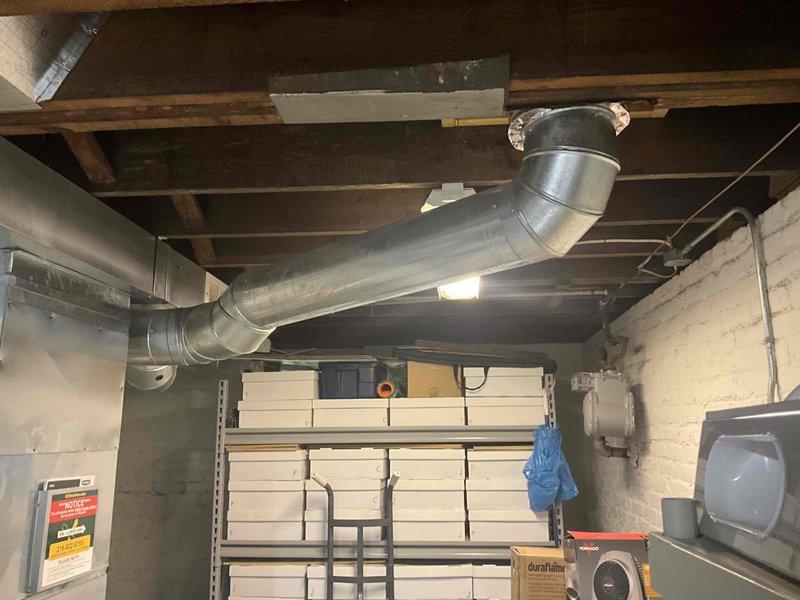 Completed estimate for ductwork replacement in basement utility area. Assessed existing metallic duct system with horizontal runs connected to vertical rectangular plenum extending floor to ceiling. Evaluated condition of galvanized ductwork with reinforced bands, curved elbow joints, and ceiling-mounted register requiring replacement to restore proper airflow and system efficiency.