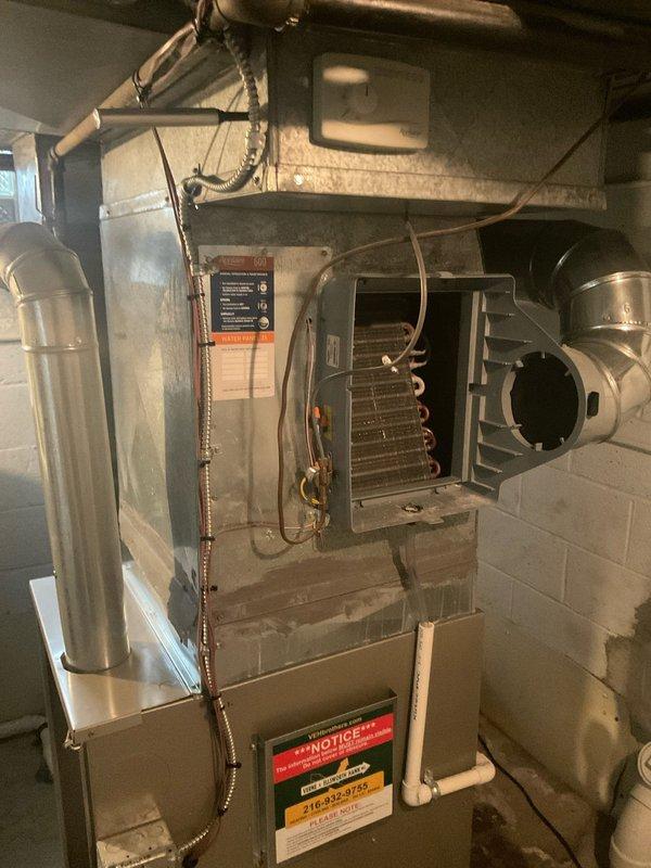 Responded to service call for air conditioning system that was completely iced over and making clanking noises. Upon arrival, found evaporator coil frozen solid with ice buildup preventing proper airflow and refrigerant circulation. Shut down system to allow coil to thaw completely, inspected internal components including finned evaporator assembly and copper refrigerant lines for damage or restrictions. Documented condition of furnace-mounted A-coil and surrounding mechanical connections with photos showing extent of ice formation and equipment configuration.