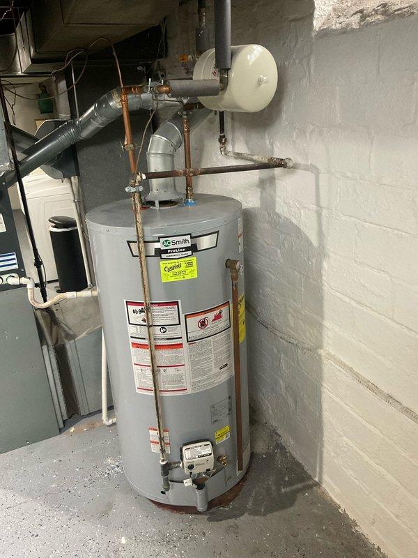Responded to service call for water heater making hissing sound and actively leaking. Upon arrival, inspected AO Smith tanked water heater in basement utility area of ninety-year-old residential property. Assessed unit condition, copper supply piping, expansion tank, and associated valves and fittings. Documented existing installation with photographs showing water heater configuration, plumbing connections, and surrounding utility infrastructure including PVC drainage and metal piping penetrations through foundation walls. Identified source of hissing and water leak, evaluated overall system integrity and functionality.