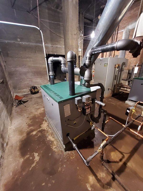 Installed new steam gas boiler with turquoise green top panel to control third floor heating system, including backflow preventer, automatic water feeder, thermostat, and main steam vent in corner location. Constructed matching concrete base pad to align with existing adjacent boiler installation and upgraded steam header from 3" to 4" black pipe to meet proper sizing requirements. Removed vaporstat from previously installed boiler and replaced with standard pressure control, leaving original vaporstat onsite for customer retention.