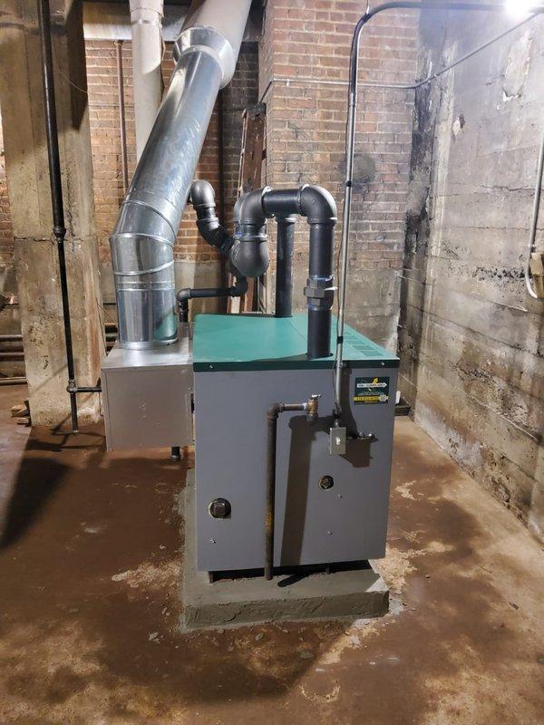 Installed new steam gas boiler with turquoise green top panel to control third floor heating system, including backflow preventer, automatic water feeder, thermostat, and main steam vent in corner location. Constructed matching concrete base pad to align with existing adjacent boiler installation and upgraded steam header from 3" to 4" black pipe to meet proper sizing requirements. Removed vaporstat from previously installed boiler and replaced with standard pressure control, leaving original vaporstat onsite for customer retention.