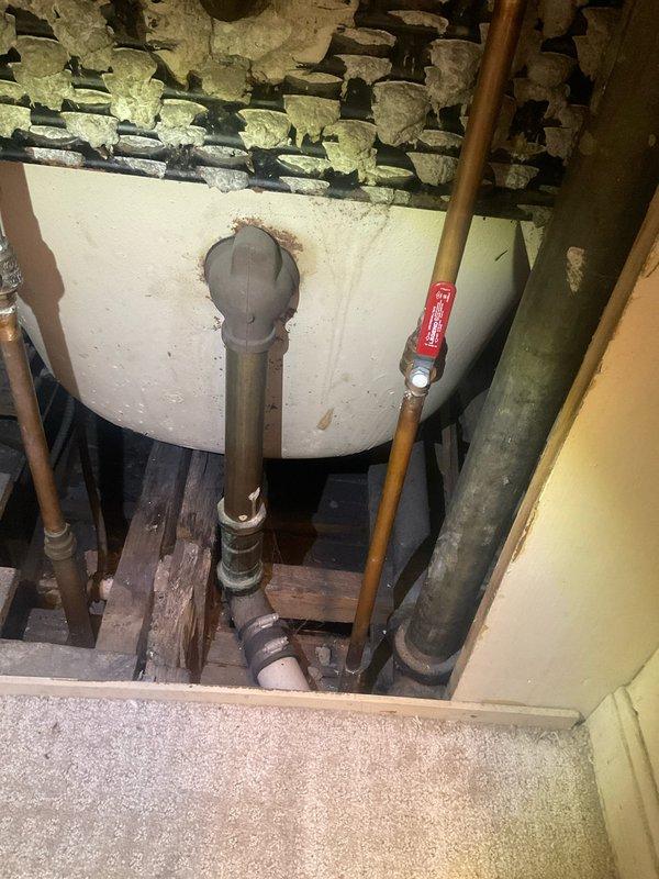 Responded to a clogged shower drain in a century-old residential property. Upon arrival, accessed the crawl space beneath the bathroom to inspect the drainage system and plumbing infrastructure. Located the main vertical drain line, which showed signs of age-related deterioration and reduced flow capacity typical of older cast iron or galvanized piping systems.

Cleared the obstruction using appropriate drain cleaning equipment and techniques suitable for vintage plumbing systems. Inspected the exposed drain line connections, PVC replacement sections, and support brackets to ensure structural integrity. Noted the presence of aging water heater and associated copper supply lines with shutoff valves in the crawl space, all showing typical wear for the home's age.

Verified proper drainage flow after clearing the blockage. Documented existing plumbing conditions including pipe materials, support systems, and overall infrastructure within the confined crawl space area. Advised homeowner on