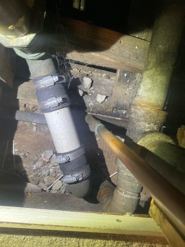 Responded to a clogged shower drain in a century-old residential property. Upon arrival, accessed the crawl space beneath the bathroom to inspect the drainage system and plumbing infrastructure. Located the main vertical drain line, which showed signs of age-related deterioration and reduced flow capacity typical of older cast iron or galvanized piping systems.

Cleared the obstruction using appropriate drain cleaning equipment and techniques suitable for vintage plumbing systems. Inspected the exposed drain line connections, PVC replacement sections, and support brackets to ensure structural integrity. Noted the presence of aging water heater and associated copper supply lines with shutoff valves in the crawl space, all showing typical wear for the home's age.

Verified proper drainage flow after clearing the blockage. Documented existing plumbing conditions including pipe materials, support systems, and overall infrastructure within the confined crawl space area. Advised homeowner on
