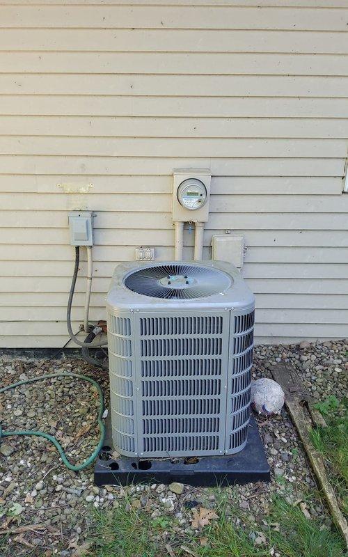 Responded to service call for non-operational air conditioning system at residential property. Upon arrival, performed comprehensive diagnostic evaluation of outdoor condensing unit, which appeared to be a cylindrical configuration with vertical fin design. Conducted visual inspection of electrical connections, disconnect box, and meter assembly mounted on exterior wall. Assessed condenser pad placement and gravel base for proper drainage and levelness. Documented equipment condition through photographic records showing unit positioning, electrical service connections, and overall installation setup. System evaluation completed and findings communicated to property occupant.