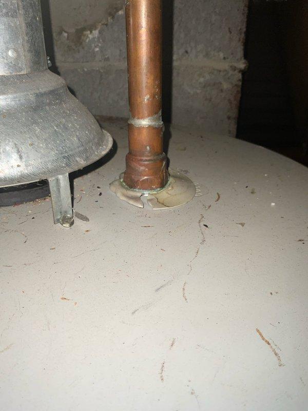 Responded to water heater leak in 70-75 year old residential property. Upon inspection, found existing Lochinvar tanked water heater with active leak at copper pipe penetration point through floor panel. Assessed plumbing infrastructure in basement utility area, including copper supply lines, valve connections, and proper venting configuration. Addressed leak source and verified all connections, fittings, and seals were secure to prevent further water damage.