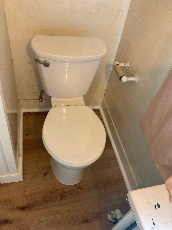 Removed toilet and chipped away concrete around flange to access subfloor structure. Installed support boards beneath flange and additional blocking to reinforce bottom side of drain elbow. Reinstalled toilet with new wax ring, secured mounting bolts, and applied silicone bead around base. Performed leak test and operational check, verified no rocking or movement of fixture.