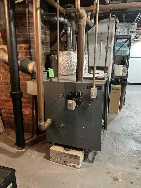 Conducted boiler replacement estimate for aging but operational heating system. Assessed existing dark gray furnace unit in basement mechanical room, documenting current installation including associated piping, ductwork connections, and ancillary HVAC equipment. Photographed equipment configuration and provided replacement recommendations for proactive system upgrade.