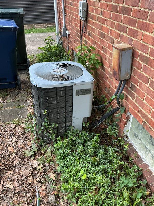 Arrived on-site to assess existing HVAC system for replacement estimate. Evaluated outdoor air conditioning unit positioned against brick wall, noting vegetation overgrowth around condenser requiring clearance for proper airflow and serviceability. Inspected indoor furnace installation in basement, including ductwork, plenum connections, and associated piping. Documented equipment conditions and took photographs of both outdoor and indoor units to support replacement proposal.