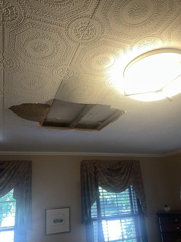 Responded to emergency service call for A/C unit in finished attic space leaking water through ceiling, causing significant structural damage and partial ceiling collapse. Upon inspection, located Carrier HVAC system in attic crawl space and assessed condensate drainage system for blockages or failures. Documented extensive ceiling damage in living area below unit, including compromised decorative plaster and exposed backing material, and photographed equipment installation including furnace unit, ductwork, PVC condensate piping, and condensate pump to identify source of water intrusion.