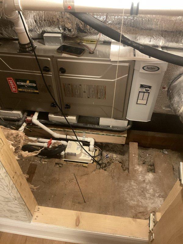 Responded to emergency service call for A/C unit in finished attic space leaking water through ceiling, causing significant structural damage and partial ceiling collapse. Upon inspection, located Carrier HVAC system in attic crawl space and assessed condensate drainage system for blockages or failures. Documented extensive ceiling damage in living area below unit, including compromised decorative plaster and exposed backing material, and photographed equipment installation including furnace unit, ductwork, PVC condensate piping, and condensate pump to identify source of water intrusion.