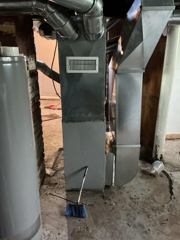 Conducted comprehensive assessment of existing furnace system located in unfinished basement area for replacement estimate. Documented current HVAC unit configuration, including vertical furnace installation with multiple branch ductwork connections and return air grille. Evaluated existing ductwork infrastructure, noted exposed metallic distribution system extending across ceiling joists, and assessed flexible duct connections to primary unit. Photographed furnace cabinet with access panel open to document internal burner assembly and control components for replacement specifications. Property was unoccupied at time of inspection, accessed via lockbox per arrangement.