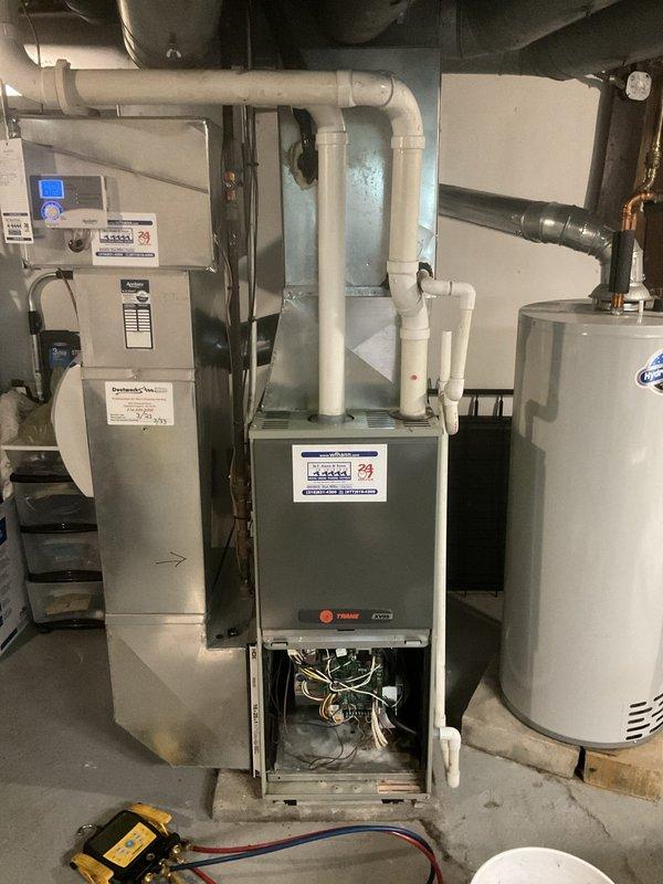 Completed annual air conditioning maintenance on a 23-year-old cooling system. Performed comprehensive inspection of the Trane furnace and associated HVAC components, including visual examination of internal wiring, electrical connections, and mechanical components with lower access panel removed for thorough access. Verified proper operation of humidifier/air handler unit and associated control systems. Inspected ductwork installation including black flexible insulated ducts and support systems throughout the mechanical space. Checked PVC condensate drainage system for proper flow and configuration, ensuring all connections and routing were secure and functional. Tested system electrical components using multimeter to verify proper voltage and amperage readings. Confirmed all equipment operating within manufacturer specifications for the cooling season.