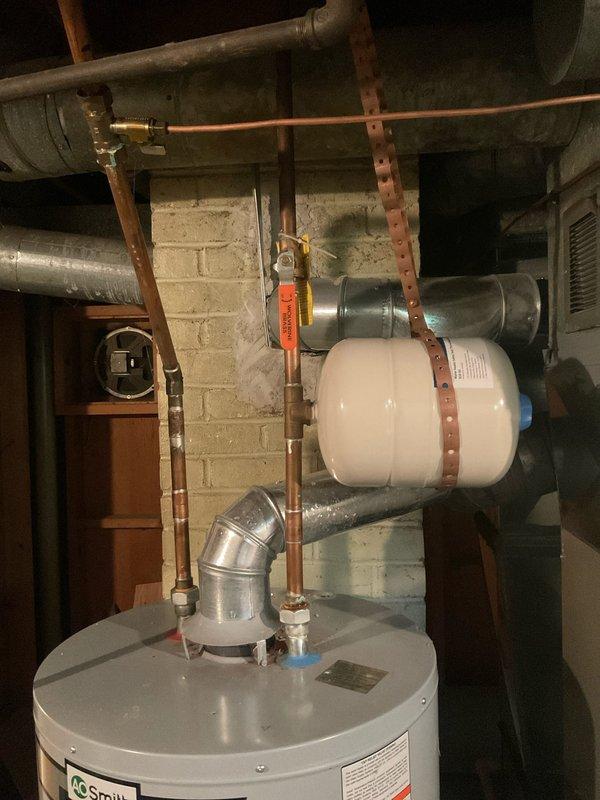 Responded to service call for faulty expansion tank on residential water heater system. Upon arrival, inspected A.O. Smith tanked water heater unit and confirmed expansion tank had failed and required replacement. Shut off water supply using existing shut-off valve and relieved system pressure. Removed old expansion tank from wall-mounted position using copper strapping brackets. Installed new expansion tank, securing it horizontally to concrete block wall with appropriate mounting hardware. Connected expansion tank to hot water system via copper piping, ensuring proper orientation and secure soldered joints. Verified all connections for leaks and proper operation. Restored water supply and brought system back online. Tested expansion tank function and confirmed proper pressure relief capability. System operating normally with new expansion tank properly absorbing thermal expansion from water heater.