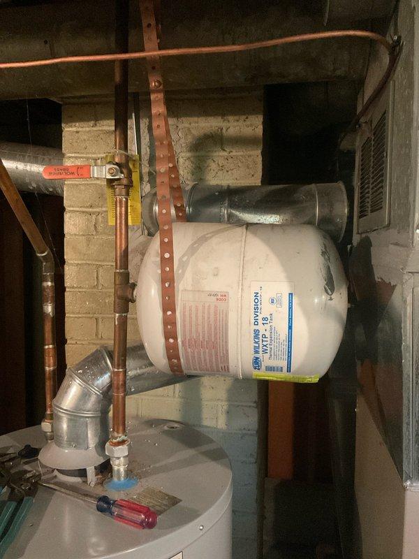 Responded to service call for faulty expansion tank on residential water heater system. Upon arrival, inspected A.O. Smith tanked water heater unit and confirmed expansion tank had failed and required replacement. Shut off water supply using existing shut-off valve and relieved system pressure. Removed old expansion tank from wall-mounted position using copper strapping brackets. Installed new expansion tank, securing it horizontally to concrete block wall with appropriate mounting hardware. Connected expansion tank to hot water system via copper piping, ensuring proper orientation and secure soldered joints. Verified all connections for leaks and proper operation. Restored water supply and brought system back online. Tested expansion tank function and confirmed proper pressure relief capability. System operating normally with new expansion tank properly absorbing thermal expansion from water heater.