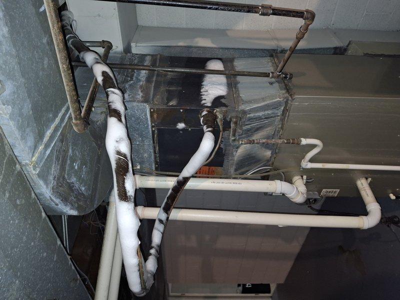 Responded to no cooling complaint on residential air conditioning system over 10 years old. Upon arrival, found outdoor condenser unit operational but indoor evaporator coil frozen with active water leakage from condensate system. Inspected airflow pathways and refrigerant circuit, documented equipment condition and drainage configuration with overgrown vegetation around outdoor unit potentially restricting airflow. System exhibited symptoms consistent with reduced airflow or low refrigerant charge causing coil freeze-up and subsequent water discharge.