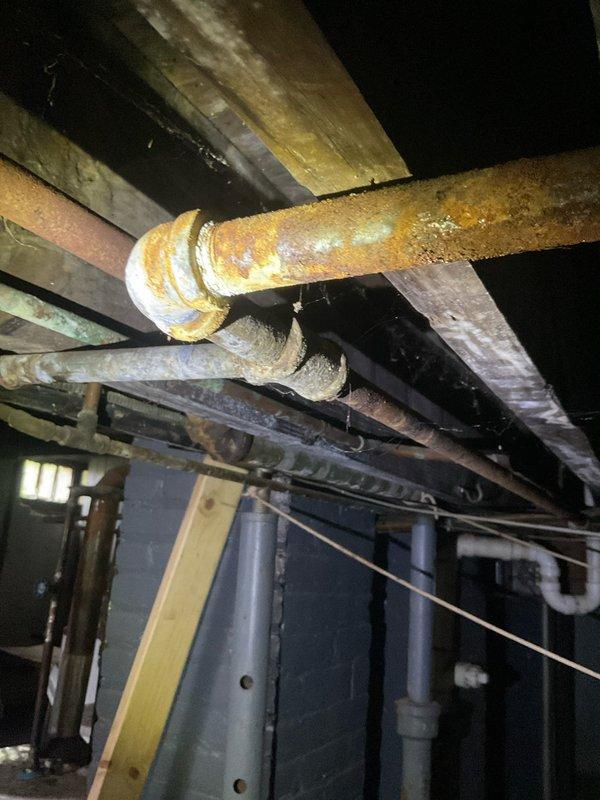 Responded to gas leak call at apartment unit 4. Upon arrival, inspected gas piping system in basement/crawlspace area and identified compromised section of gas line with hole requiring immediate repair. Located leak in heavily corroded steel gas pipe with significant rust deterioration throughout visible piping infrastructure. Documented existing conditions with photos showing extensive oxidation on threaded connections, unions, and pipe surfaces. Assessed structural environment including floor joists and surrounding utility systems. Identified safety hazard requiring prompt attention to restore gas service integrity and eliminate leak risk. Repair work needed on damaged section of gas line to address hole and restore safe operation of gas system.