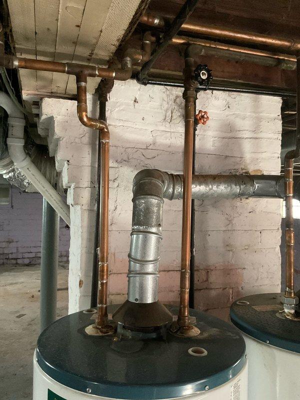 Responded to service call for insufficient hot water production from recently installed tanked water heater system. Upon arrival, found dual water heater configuration in basement utility area with copper supply lines and galvanized venting. Customer reported only lukewarm water available despite new installation. Performed diagnostic inspection of both units, examining temperature settings, gas supply connections, burner operation, and flue venting system. Inspected copper piping connections for proper flow and potential cross-connections that could affect water temperature. Evaluated vent pipe assembly and draft hood for proper combustion air flow and exhaust. Checked pressure relief valves, dip tubes, and internal heating elements for proper function. Documented existing plumbing configuration showing aged copper piping with oxidation, galvanized vent connections, and installation in unfinished basement space with exposed joists. Identified issues preventing adequate hot water deliv