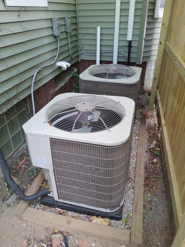 Responded to no cooling call for one-year-old residential AC system affecting entire home. Upon arrival, accessed outdoor condensing units located in side yard between house and fence. Performed diagnostic inspection of dual outdoor units positioned on rubber isolation pads with proper clearances. Visually inspected condenser coils, fan grilles, electrical connections, and refrigerant line sets. Verified both units were properly mounted on concrete bases with adequate drainage. Checked wire grille protective covers and heat exchanger assemblies for any visible damage or obstructions. System components appeared in normal operating condition with no obvious mechanical failures or debris blockage visible on exterior equipment.