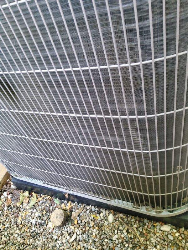 Responded to no cooling call for one-year-old residential AC system affecting entire home. Upon arrival, accessed outdoor condensing units located in side yard between house and fence. Performed diagnostic inspection of dual outdoor units positioned on rubber isolation pads with proper clearances. Visually inspected condenser coils, fan grilles, electrical connections, and refrigerant line sets. Verified both units were properly mounted on concrete bases with adequate drainage. Checked wire grille protective covers and heat exchanger assemblies for any visible damage or obstructions. System components appeared in normal operating condition with no obvious mechanical failures or debris blockage visible on exterior equipment.