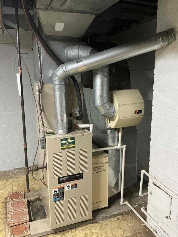 Provided comprehensive estimate for complete HVAC system replacement of aging 19+ year old furnace and air conditioning equipment. Evaluated existing basement-installed furnace with associated ductwork, humidifier, and outdoor condenser unit positioned on concrete pad against exterior wall. Assessed current system configuration including galvanized metal ductwork, copper refrigerant lines, PVC condensate drainage, and electrical disconnect components to determine replacement specifications and installation requirements for new high-efficiency heating and cooling system.