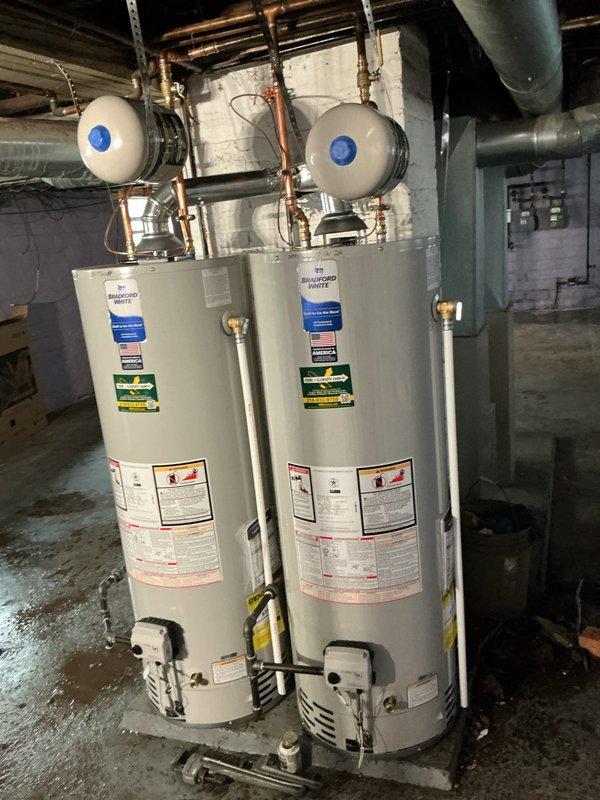 Removed existing flue piping and enlarged chimney penetration to accommodate 5-inch flue system. Installed 5x3x3 wye fitting and connected to multiple water heater units, sealing chimney penetration with furnace cement per code requirements. Completed water line bonding to establish proper electrical grounding of plumbing system as mandated by code. Replaced existing expansion tank with new unit to ensure proper thermal expansion control for the water heating system.