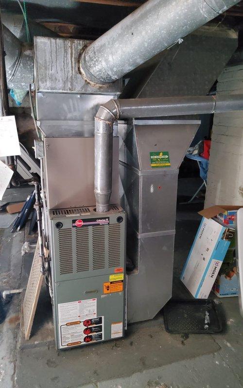 Responded to emergency no-cooling call for residential air conditioning system of unknown age. Upon arrival, performed diagnostic assessment of outdoor condensing unit and indoor air handler/furnace system. Inspected Rheem furnace and associated ductwork in basement utility area, verifying proper connections and airflow pathways. Evaluated outdoor AC unit positioned on concrete pad against exterior wall, checking for operational issues and proper installation. Documented equipment condition through photographic records showing both indoor HVAC components and exterior condensing unit. System assessed and emergency service completed to restore cooling functionality to residence.