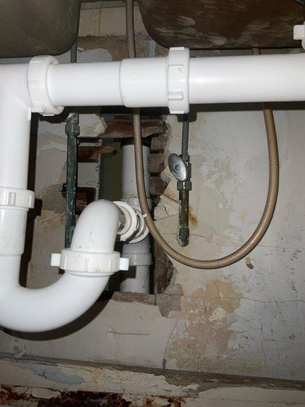 # Kitchen Sink Drain Follow-Up Service

Responded to a follow-up service call for a kitchen sink drain issue in a 104-year-old residential property. Upon arrival, coordinated access with the tenant after confirming with the property contact. 

Inspected the double-basin stainless steel kitchen sink and associated drain assembly. Found existing white PVC P-trap and drain piping installed beneath the sink, integrated with older metal plumbing infrastructure typical of the home's 1922 construction. The drain system showed signs of previous repairs with mixed materials including newer plastic fittings connected to legacy metal components.

Evaluated the complete drainage pathway from both sink basins through the P-trap assembly. Assessed the horizontal drain pipe connection and verified proper trap configuration to ensure adequate water seal. Examined the condition of all visible plumbing connections, including the interface points between the modern PVC components and the older metal pipi