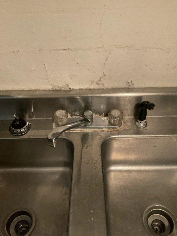 # Kitchen Sink Drain Follow-Up Service

Responded to a follow-up service call for a kitchen sink drain issue in a 104-year-old residential property. Upon arrival, coordinated access with the tenant after confirming with the property contact. 

Inspected the double-basin stainless steel kitchen sink and associated drain assembly. Found existing white PVC P-trap and drain piping installed beneath the sink, integrated with older metal plumbing infrastructure typical of the home's 1922 construction. The drain system showed signs of previous repairs with mixed materials including newer plastic fittings connected to legacy metal components.

Evaluated the complete drainage pathway from both sink basins through the P-trap assembly. Assessed the horizontal drain pipe connection and verified proper trap configuration to ensure adequate water seal. Examined the condition of all visible plumbing connections, including the interface points between the modern PVC components and the older metal pipi